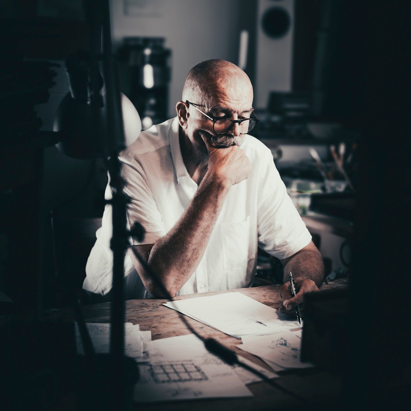 Prof. Andrzej Bednarczyk w białej koszuli zamyślony przy biurku w pracowni, portret artysty