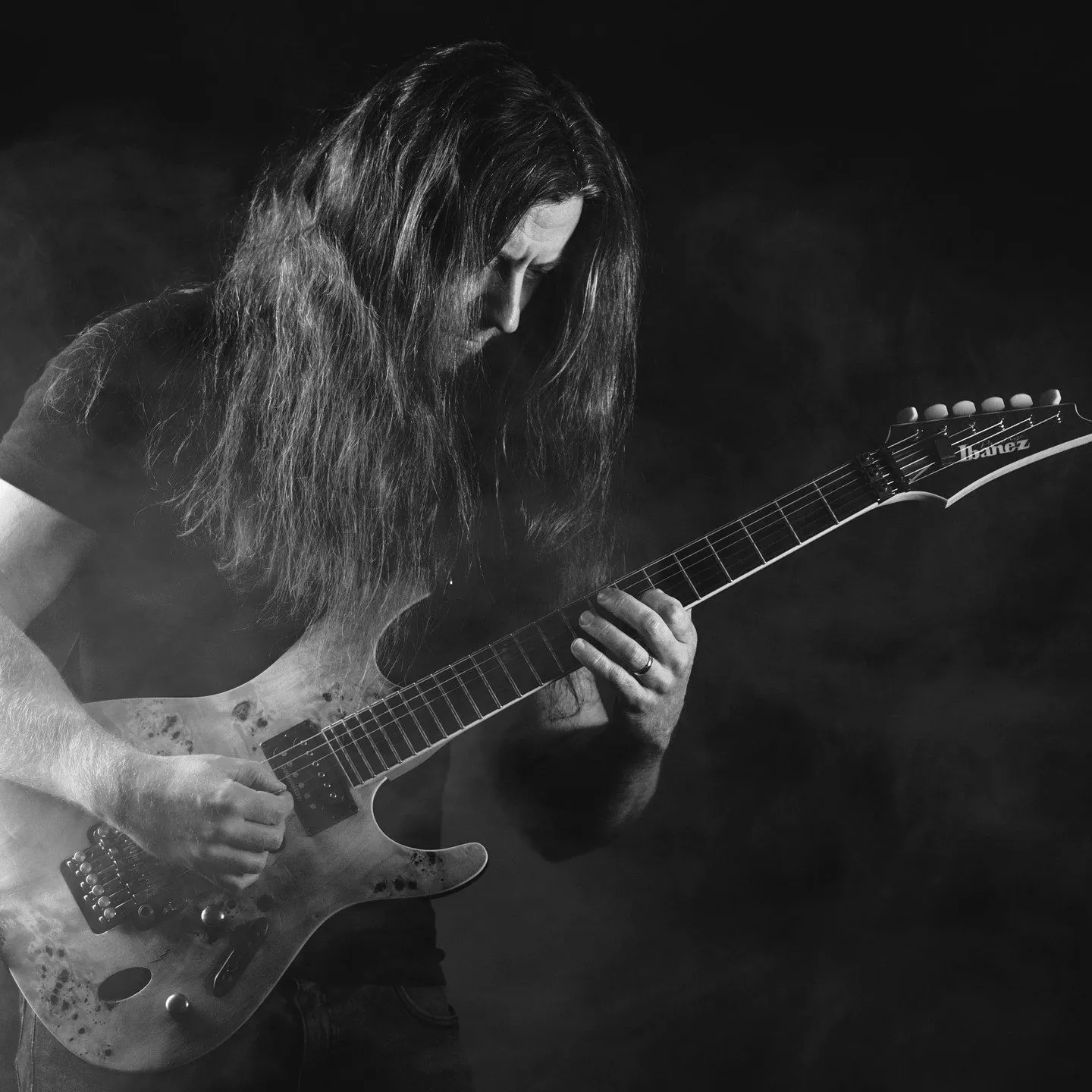 Portret artystyczny gitarzysty z długimi włosami grającego w dymie, czarno-białe zdjęcie promocyjne muzyka