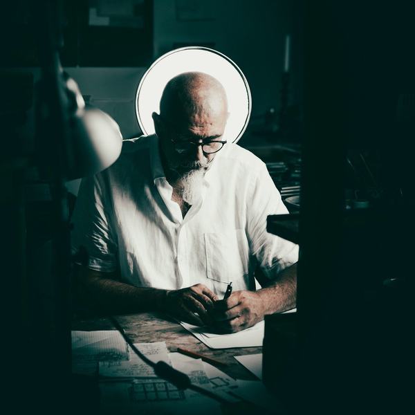 Artysta przy stole kreślarskim w pracowni, portret środowiskowy w półmroku