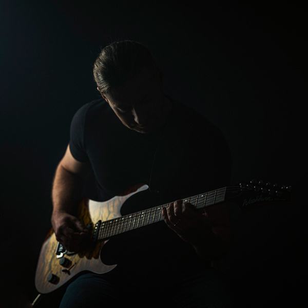Muzyk z gitarą w ciemnym studiu, światło konturowe, sesja wizerunkowa muzyka, studio w Katowicach