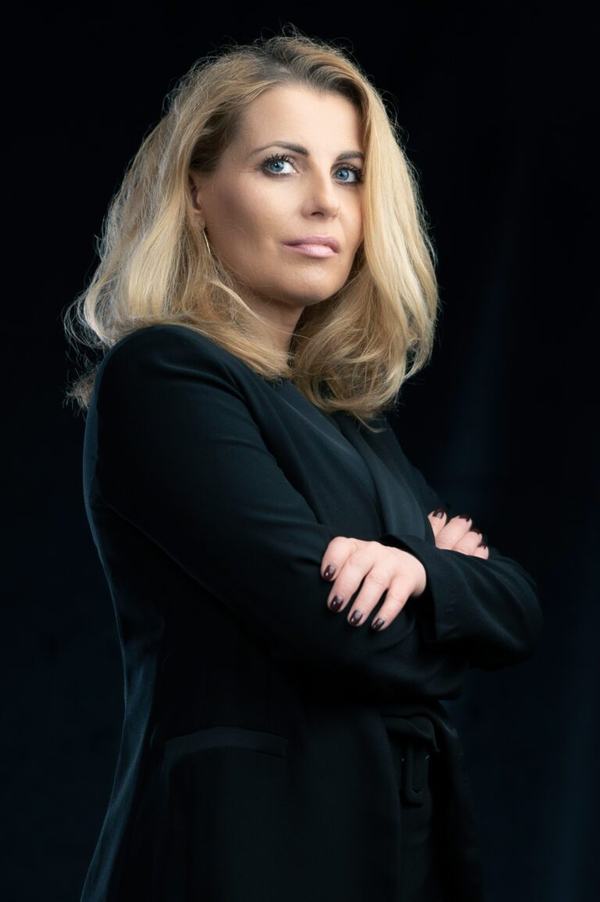 Portret biznesowy: blondynka w ciemnej marynarce z rękami skrzyżowanymi