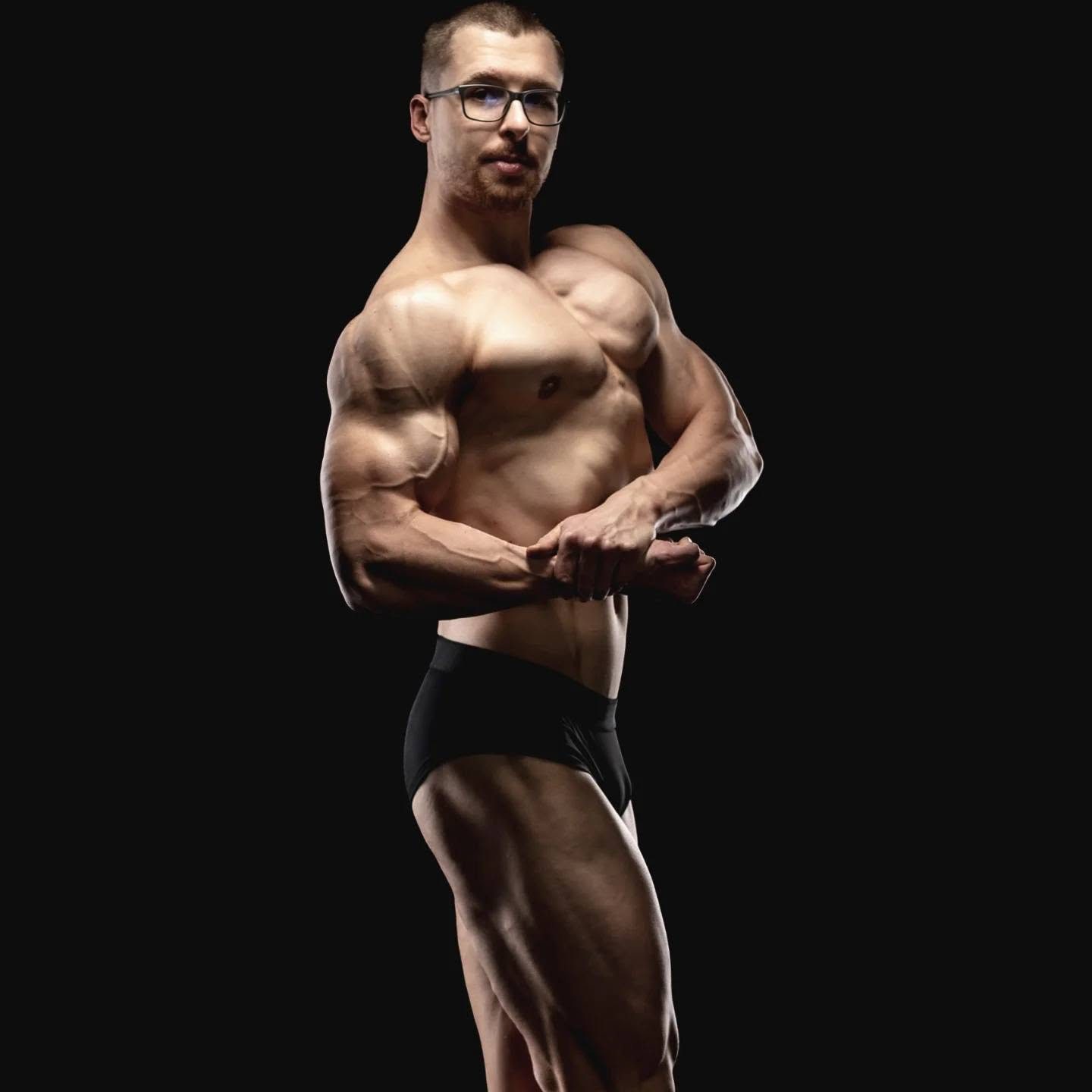 Sesja wizerunkowa trenera personalnego: cała sylwetka w pozie side chest na czarnym tle