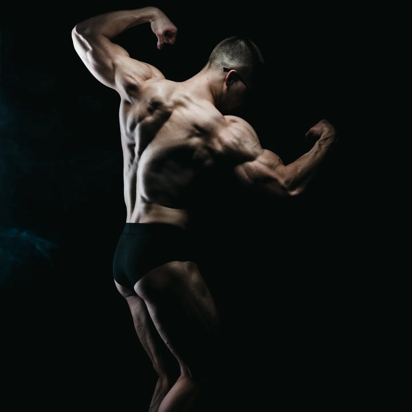Sesja fitness trenera personalnego: poza double biceps tyłem na ciemnym tle